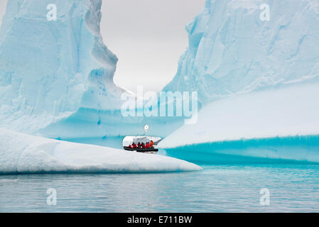 Persone in zodiac barche di nervatura passando da torreggianti iceberg sulla calma acqua circa le piccole isole della penisola antartica. Foto Stock