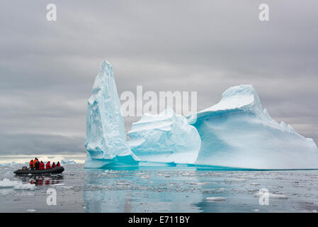 Le persone in piccoli inflatible zodiac barche di nervatura passando da torreggianti scolpito iceberg intorno le piccole isole della penisola antartica. Foto Stock