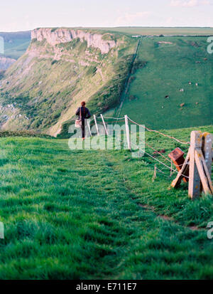 Una donna che cammina lungo una linea di recinzione sulla cima di una scogliera percorso. Vista del paesaggio. Foto Stock