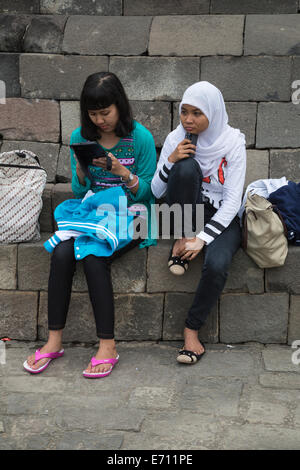 Borobudur, Java, Indonesia. Due giovani ragazze indonesiane con un telefono cellulare e il tuo iPad. Foto Stock