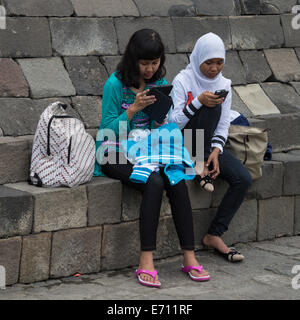 Borobudur, Java, Indonesia. Due giovani ragazze indonesiane con un telefono cellulare e il tuo iPad. Foto Stock