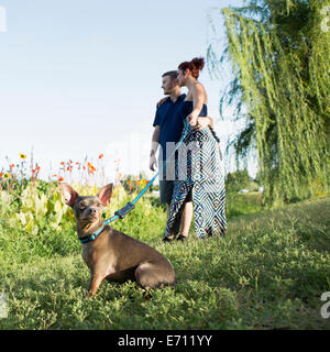 Un giovane nel parco con un piccolo cane su un filo blu. Foto Stock