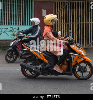 Yogyakarta, Java, Indonesia. La sicurezza stradale. Bambina succhiare il suo pollice mentre equitazione con sua madre su una moto. Foto Stock