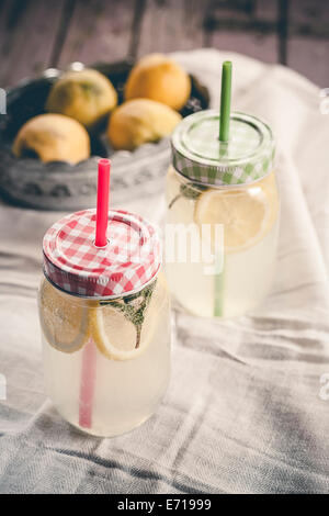 Due vite-top vasetti di limone e menta infuso di acqua e una ciotola di limoni su tela Foto Stock