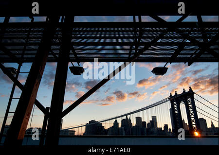 Vista di Manhattan Bridge al tramonto da Brooklyn tetto, incorniciato dalla struttura tramite affissioni in primo piano. Foto Stock