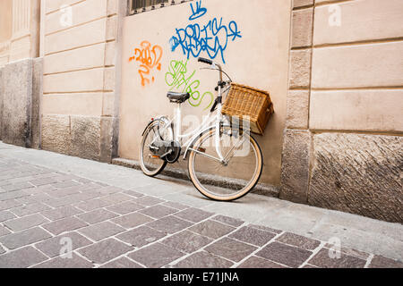 Bicicletta retrò appoggiata contro la parete sotto la bomboletta spray graffiti di atti di vandalismo. Foto Stock