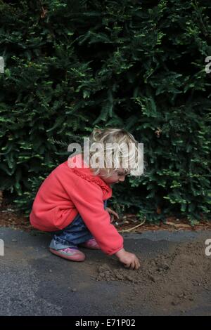 Un bambino piccolo squatting e giocare con lo sporco sul terreno. Foto Stock