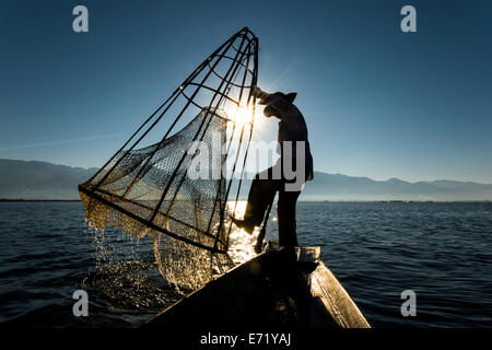 Fisherman nella luce del mattino, con un tradizionale cestello sul canoa, all'alba, Lago Inle, Stato Shan, Myanmar Foto Stock