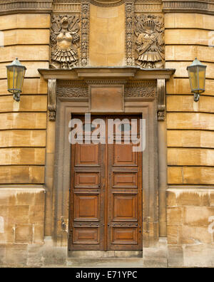 Ornati in legno marrone doppie porte con pannelli rettangolari e altamente decorativi in pietra scolpita frame nella parete di edificio storico a Oxford, Inghilterra Foto Stock