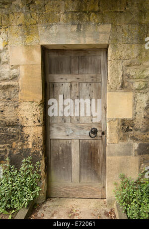 Weathered marrone porta in legno nel muro di pietra del palazzo storico con fogliame verde in corrispondenza di ciascun lato della porta in Oxford, Inghilterra Foto Stock