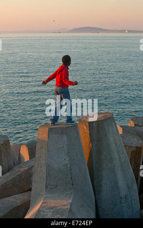 Ragazzo di gettare un sasso presso il Victoria & Alfred Waterfront frangionde Foto Stock