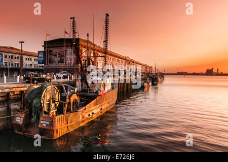 Il sole sorge su Logan International Airport, l'illuminazione delle barche da pesca ormeggiate lungo il molo del pesce nel quartiere portuale Foto Stock