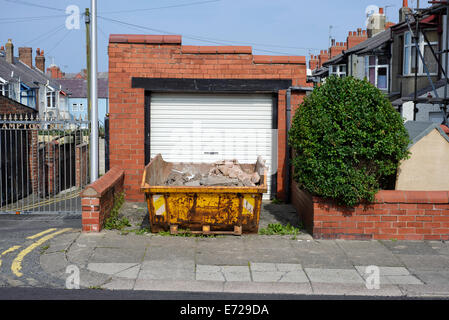 Saltare contenente costruttori macerie al di fuori di un garage in Blackpool Lancashire Foto Stock