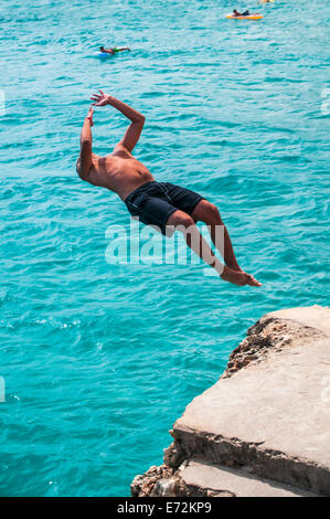 Giovane uomo facendo un backward flip da una scogliera sul mare vicino a Calas de Mallorca Foto Stock