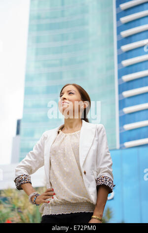 Ritratto di felice e comunque fiduciosi latina imprenditrice in tailleur, guardando fiduciosi al grattacielo e edifici per uffici in t Foto Stock