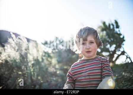 Un giovane ragazzo guarda verso la telecamera con il sole che splende in background mentre si trova al di fuori di escursionismo. Foto Stock