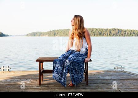 Vista della ragazza adolescente (16-17) seduto accanto al fiume Foto Stock