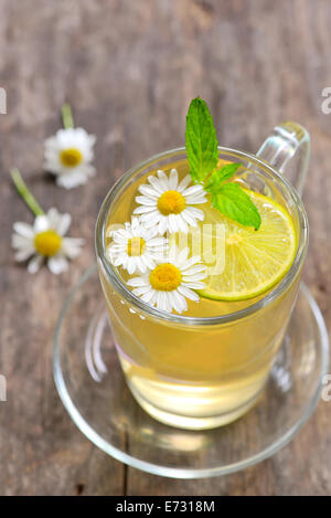 Il tè alle erbe con freschi Fiori di camomilla e limone su sfondo di legno Foto Stock