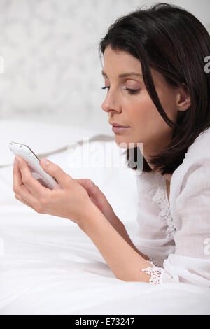 Donna sdraiata sul letto con telefono Foto Stock