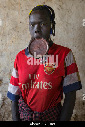 Tribù dei Mursi donna con un labbro di piastra e un arsenale Tshirt, grandine Wuha Village, Etiopia Foto Stock