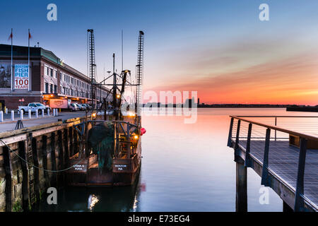 Il sole sorge su Logan International Airport, l'illuminazione delle barche da pesca ormeggiate lungo il molo del pesce nel quartiere portuale Foto Stock