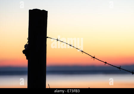 Silhouette di barb filo in un post al tramonto con il cielo colorato Foto Stock