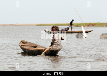 Africa, Benin, Ganvie. Giovane donna paddling piroga con reti da pesca in background. Foto Stock