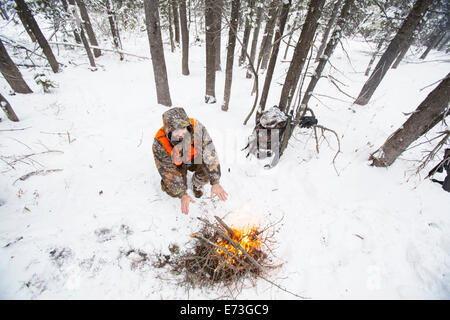 Un cacciatore maschio rimane caldo accanto a un incendio nella neve. Foto Stock