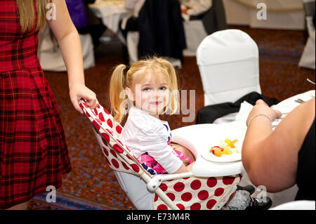 Damigella bambina seduta nel seggiolone a un ricevimento di nozze godendo di pasto Foto Stock