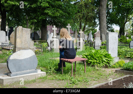 Dolore donna accartocciati vicino a padre marito tomba nel cimitero. Foto Stock