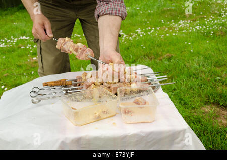 L'uomo messo ordinatamente verde infilza carne di maiale preparato per la cottura a fuoco Foto Stock