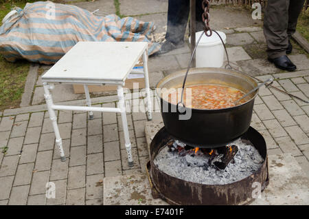 Big black metal vecchia pentola piena di stile rustico zuppa di verdure su un fuoco aperto all'aperto Foto Stock