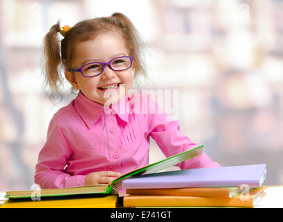 Bambino felice ragazza in occhiali lettura di libri seduta a tavola Foto Stock