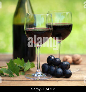 Vino rosso su una tavola di legno in una bottiglia e due bicchieri. Messa a fuoco selettiva sul vetro in primo piano. Foto Stock