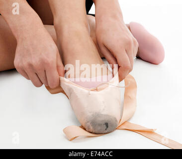 Close-up di mani e gambe di una ballerina seduta sul pavimento e la messa su raso ballet pantofole, preparazione per perfo Foto Stock