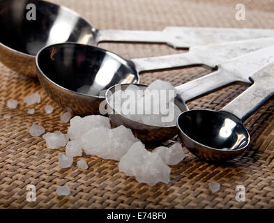 Il sale di mare in un metallo cucchiai su un tampone di legno. Foto Stock