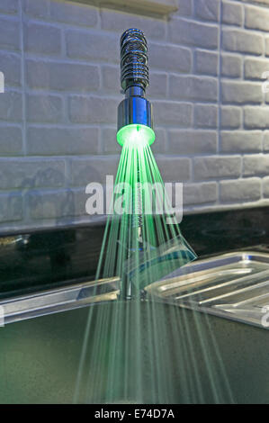 Ornati di lusso illuminato tocca il rubinetto con luce verde e acqua in esecuzione in appartamento cucina Foto Stock
