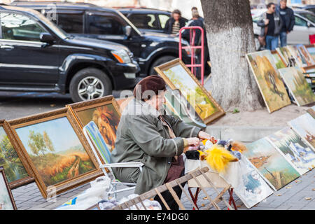 Vecchia donna seduta in strada vendere dipinti, foto e peluche ai turisti come souvenir a Kiev, Ucraina Foto Stock