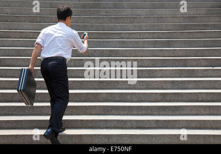 Imprenditore azienda mobile e in fretta per correre su scale Foto Stock