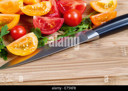 Primo piano immagine orizzontale di coltello da cucina e affettare i pomodori e il prezzemolo bamboo naturale tagliere Foto Stock