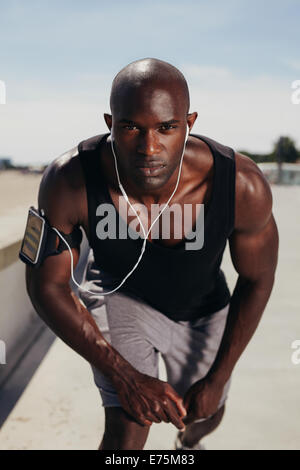 Montare il giovane ragazzo sul suo marchio per iniziare una corsa. Focalizzato giovane atleta maschio all'esterno guardando la fotocamera. Africa muscolare modello maschile. Foto Stock