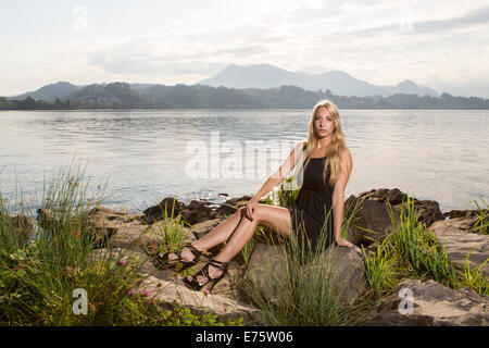 Donna che indossa un abito nero seduto su una riva del lago Foto Stock