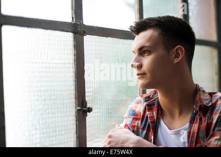 Giovane uomo che guarda fuori da una finestra Foto Stock