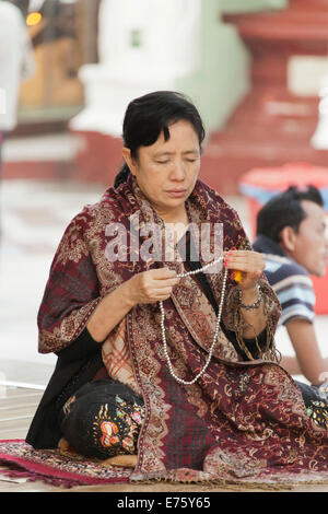 Donna buddista nella preghiera del mattino presso la Shwedagon pagoda, con grani di preghiera, Yangon, Myanmar Foto Stock