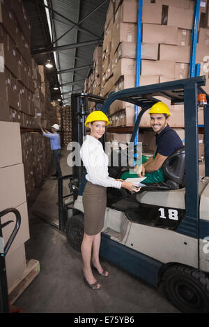 Responsabile magazzino sorridente in telecamera con driver di carrello elevatore a forche Foto Stock