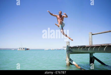 Giovane salta fuori il dock in legno in acqua Foto Stock