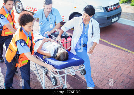 Medico, infermiere e personale paramedico wheeling paziente sul lettino Foto Stock