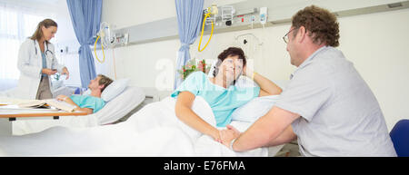 Uomo che parla alla moglie nella stanza di ospedale Foto Stock