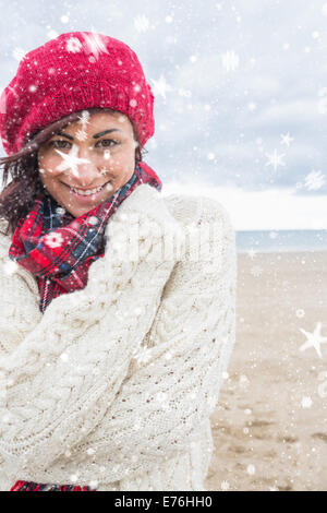 Immagine composita di carino donna sorridente in eleganti abiti caldi sulla spiaggia Foto Stock