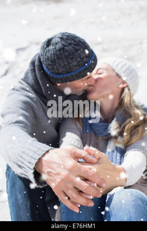 Immagine composita della coppia attraente baciare sulla spiaggia in un abbigliamento caldo Foto Stock